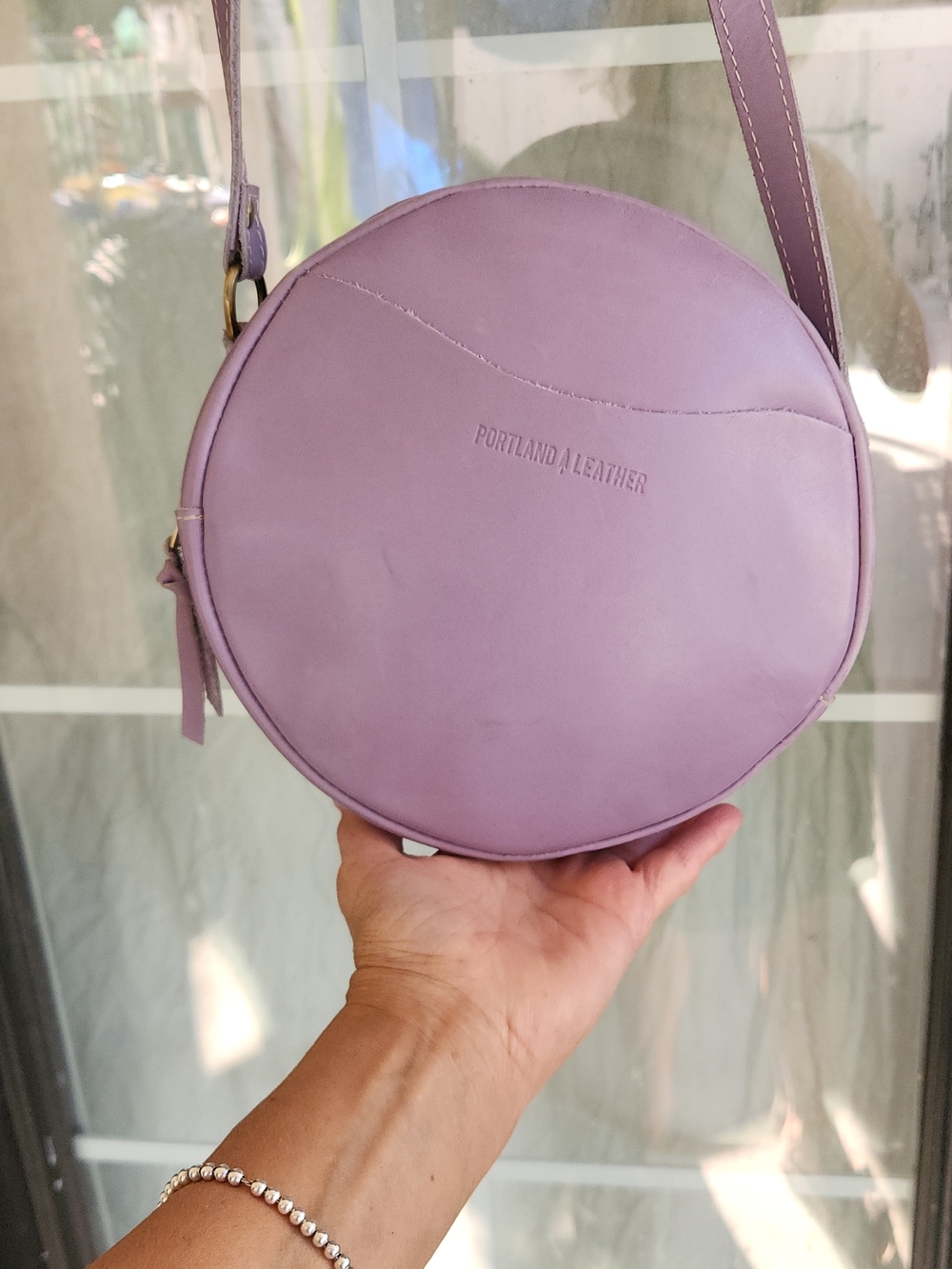 The purple round bag in the image is a Circle Crossbody in the color Lavender - Picture 4 of 8